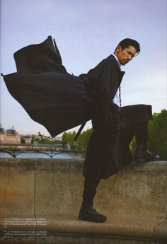 a man sitting on top of a cement wall next to a river holding an umbrella