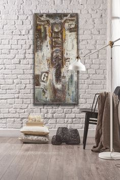 an abstract painting hangs on the wall next to a black chair and white brick wall