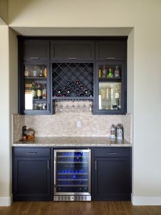 a wine cooler in the middle of a kitchen with dark cabinets and marble counter tops