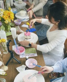 a group of people sitting around a table with cakes on it and flowers in vases