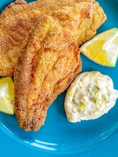 two fried fish fillets on a blue plate with lemon wedges and mayonnaise