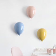 three balloons are hanging on the wall above a dining room table with two pink chairs