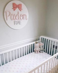 a white crib with a pink teddy bear in it and a sign that says poxton rac on the wall