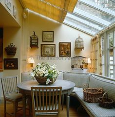 a table with flowers on it in front of a couch and some pictures hanging on the wall