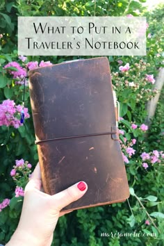 a hand holding an old leather traveler's notebook in front of purple flowers with the title what to put in a traveler's notebook