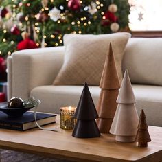 three christmas trees sitting on top of a coffee table next to a book and candle