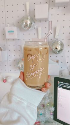 a person holding up a cup of coffee in front of a computer screen and christmas decorations