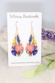 a pair of earrings with flowers on them sitting next to some purple and yellow flowers