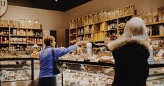 two people standing in front of a store filled with shelves full of bottles and jars