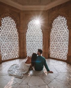 a man and woman sitting on the floor in front of an ornate wall with arched windows