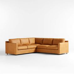 a tan leather sectional sofa with wooden legs and arm rests against a white wall in an empty room