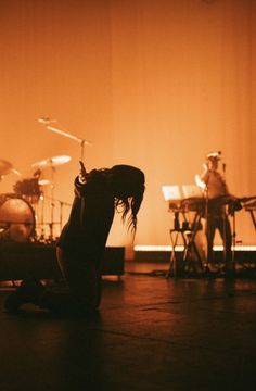 a person sitting on the floor in front of drums and drummers playing instruments behind them