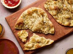 two pieces of pizza sitting on top of a wooden cutting board next to sauces