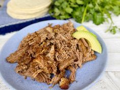 a blue plate topped with pulled pork and an avocado next to tortilla chips