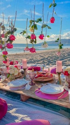 a table set up on the beach with flowers hanging from it's branches and plates