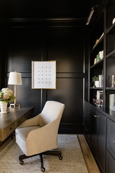 a chair in front of a desk with a lamp on it and bookshelves