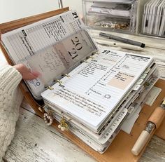 a person is holding a binder full of papers on a wooden table with pens and pencils