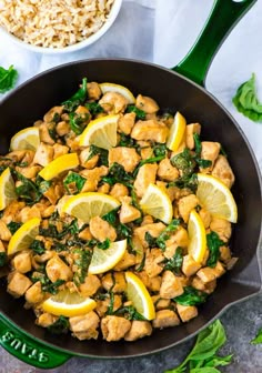 a skillet filled with chicken, spinach and lemon wedges next to rice