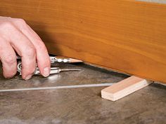 a person is using pliers to cut the edge of a piece of wood on the floor