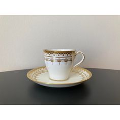 a cup and saucer sitting on top of a black table next to a white wall