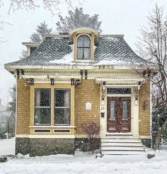 a yellow house with snow falling on the roof and steps leading up to it's front door