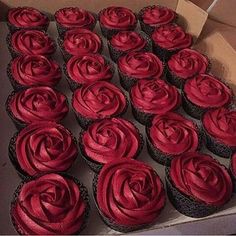 a box filled with red frosted cupcakes on top of a wooden table