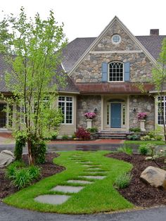 a stone house with green grass and rocks in the front yard, along with landscaping