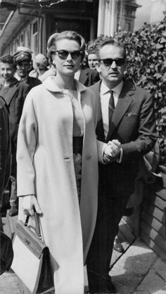 an old black and white photo of a woman in a long coat with sunglasses on