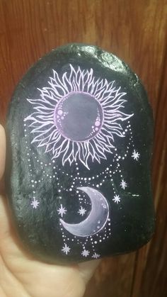 a hand holding a painted rock with the sun and moon on it