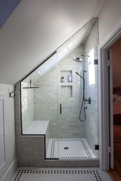 a walk in shower sitting next to a white door and tiled floor with black and white tiles on the floor