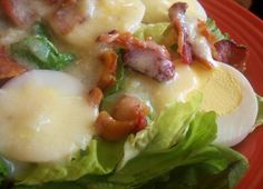 a red plate topped with lettuce covered in cheese and bacon next to a fork