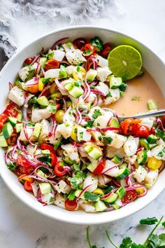 a white bowl filled with cucumber, red onion and tomato salad next to a lime wedge