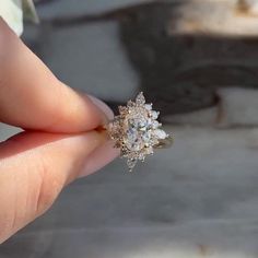 a woman's hand holding an engagement ring in front of her face, with the center diamond surrounded by smaller diamonds