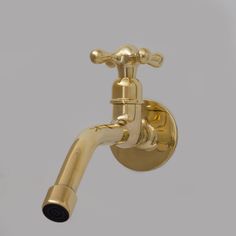 a gold faucet on the side of a white wall with a black handle