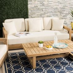 a living room with white couches and wooden tables in front of a brick wall