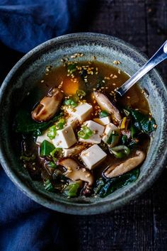 a bowl of soup with tofu, spinach and other vegetables in it on a blue cloth