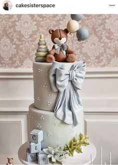 a three tiered cake with a teddy bear on top and balloons in the air