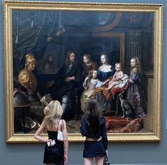 two women standing in front of a large painting with people looking at it and one is holding a purse