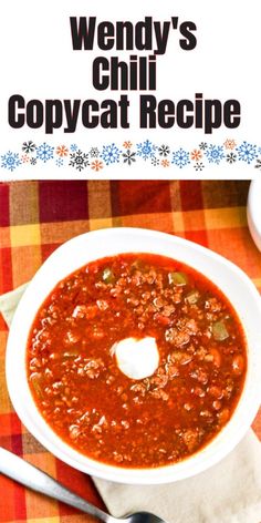 a white bowl filled with chili soup on top of a checkered table cloth next to a spoon