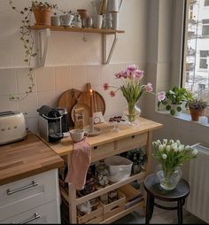 a kitchen with pots, pans and flowers on the counter next to a window