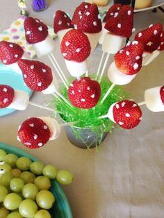 strawberries and green olives are arranged on skewers in front of a bowl of grapes