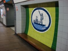 an image of a subway station with tile murals on the wall and people walking by