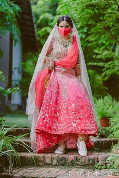 a woman in a red and pink wedding dress standing on steps with her veil over her face