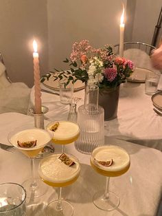 four glasses filled with drinks sitting on top of a table next to a vase full of flowers