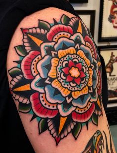 a colorful flower tattoo on the left arm and shoulder, with other tattoos in the background