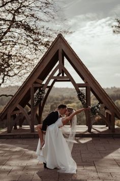 a bride and groom kissing in front of a wooden structure at their outdoor wedding venue