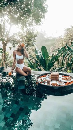 a woman sitting on the edge of a swimming pool with food in front of her