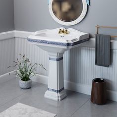 a white sink sitting under a bathroom mirror next to a potted plant and towel rack