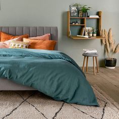 a bed with blue sheets and orange pillows in a small room next to a book shelf