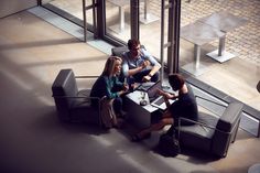 three people sitting at a table with laptops and papers in front of glass doors